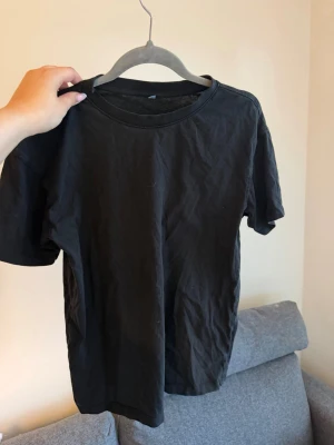 Svart basic t-shirt i bomull - En enkel svart t-shirt med rund hals och korta ärmar. Tillverkad i mjuk bomull, perfekt för en clean och avslappnad stil. Passar till allt och är ett måste i garderoben.