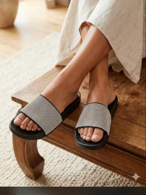 Svarta sandaler med strass från Cucucoo - Säljer ett par svarta slip-in sandaler från CUCUCOO med breda band täckta av glittrande strass. Snygg och bekväm design med mjuk sula, perfekta för att addera lite bling till din outfit. Passar till både jeans och klänning.