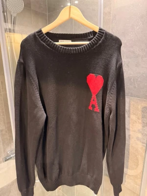 Svart stickad tröja från Ami Paris - Snygg svart stickad tröja från Ami Paris med deras ikoniska röda hjärta och A på bröstet.  Tröjan är i perfekt skick och har endast använts 1 gång. 