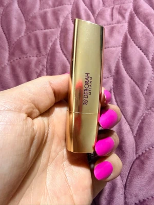 Fuchsia läppstift Deborah Milano - Snyggt fuchsiafärgat läppstift från Deborah Milano med elegant guldfärgat hylsa. Läppstiftet har en klassisk form och ger en intensiv färg till läpparna. Perfekt för dig som vill ha en färgstark look och gillar lyxig design.