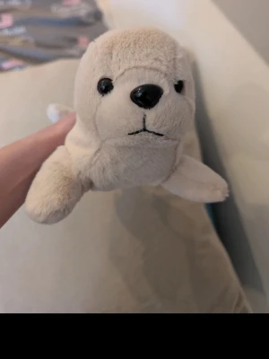 Mjukisdjur säl vit plysch - Säljer ett gulligt mjukisdjur i form av en säl, tillverkat i mjuk vit material. Den har svarta plastögon och nos samt broderad mun. Perfekt som kramkompis eller dekoration i rummet.