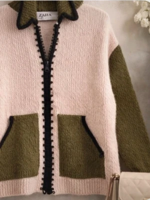 Zara stickad kofta i beige och olivgrön - Säljer en mysig stickad kofta från Zara i beige med olivgröna ärmar och fickor. Koftan har svarta detaljer längs dragkedjan och fickkanterna samt en hög krage. Perfekt för lager på lager och chill stil.