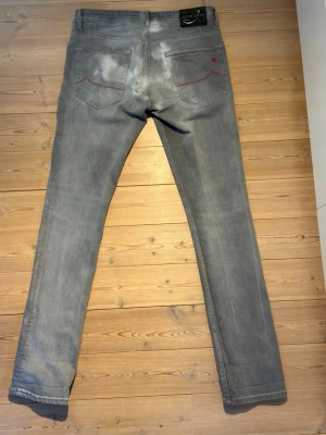 Grå slim fit jeans från Jacob Cohen - Ett par fina Jacob Choen Jeans i ljusgrå färg med en grön läderlapp baktill. Några små trådar som släppt något i övrigt bra skick. Byxorna är Slim Fit W32 Längd på  Byxben är 106 cm, Övre delen av låret 24 cm, Midje mått 41 cm. Kontakta oss vid frågor!  Skickas samma dag eller dagen efter, därefter 1-3 dagars leveranstid! P1 