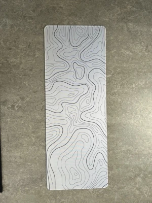 Stilren musmatta med topografiskt mönster - Säljer en avlång musmatta i vitt med svart topografiskt mönster. Mattan har rundade hörn och sydda kanter för extra hållbarhet. Perfekt för gaming eller kontorsbruk och ger skrivbordet en modern look.