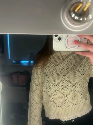 Beige stickad tröja med spetskant - Säljer en beige stickad tröja med snyggt hålmönster och ribbade muddar. Tröjan har en söt spetskant nedtill och är lite croppad i modellen. 