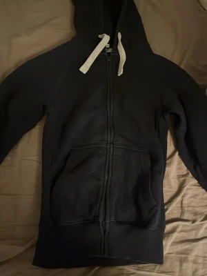 Svart zip hoodie från russemerch XS - Säljer en svart hoodie från russedress i storlek XS. Hoodien har dragkedja framtill, vita snören i huvan och en stor magficka. Perfekt för en chill och avslappnad stil. Materialet känns mjukt och bekvämt. Storlek xs men passar defensivt s om inte större.