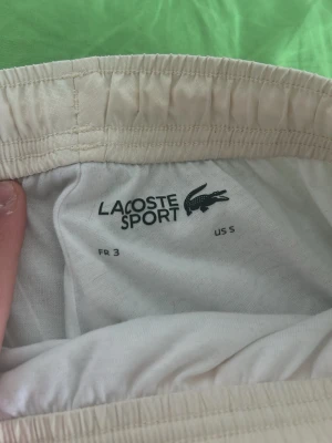 Vita byxor från  Lacoste Sport /utsläppta - Säljer ett par vita shorts från Lacoste Sport med resår i midjan. De är tillverkade i ett mjukt och lätt material som passar perfekt för träning eller chill. Klassisk design med diskret logga och enkel passform.