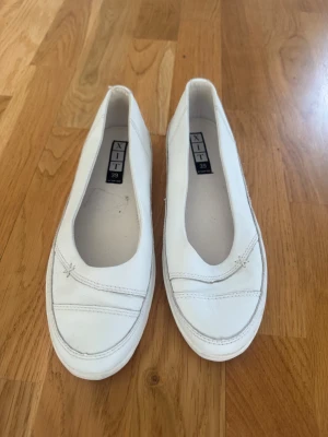 Vita ballerinaskor från XIT - Snygga vita ballerinaskor från XIT med rundad tå och diskreta sömdetaljer framtill. Skorna har en klassisk och enkel design med låg profil och är tillverkade i ett slätt material som ger en clean look. Perfekta för dig som gillar stilrena och minimalistiska skor.