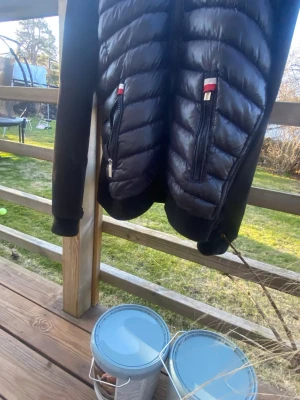 Moncler cardigan - Svart pufferjacka med quiltad front och två dragkedjeförsedda fickor med röda och vita detaljer. Ärmarna är släta och jackan har ribbade muddar. Perfekt för kalla dagar och snygg att matcha med jeans.