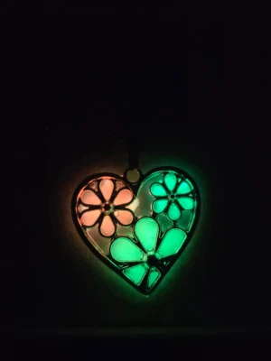 Halsband som lyser med hjärthänge och blommor  - Unikt halsband med ett hjärtformat hänge i silverfärgad metall. Hänget har färgglada blommor i rött, grönt och gult och lyser i mörkret med neonfärger. Kedjan är tunn i rostfritt stål och är justerbar. Perfekt för dig som gillar färg och coola detaljer. 