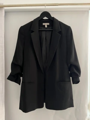 Svart oversized kavaj från H&M - Stilren svart oversized kavaj från H&M med två framfickor och trekvartsärmar. Tillverkad i ett slätt tyg som ger en snygg och modern look. Inga synliga defekter😊