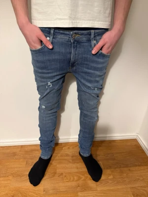 Slim fit jeans Jack&jones  - Säljer ett par blå slimfit jeans med slitningar och lätt tvättad look. Jeansen har klassisk femficksmodell och bra passform. Perfekta för dig som gillar en trendig och avslappnad stil. Pris kan diskuteras!💸 Strl: W30 L34 men passar W30 L32✅ Hör av dig om du har funderingar!👍