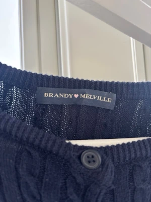 Mörkblå kofta - Snygg mörkblå kabelstickad kofta från Brandy Melville med knappar framtill. Koftan har en klassisk rund halsringning och ribbade muddar. Endast testad