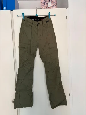 Olivgröna cargobyxor från Urban Classics - Säljer ett par olivgröna cargobyxor med raka ben och flera praktiska fickor på sidorna. Byxorna har klassisk cargomodell med knapp- och dragkedjegylf samt förstärkta sömmar. Perfekta för en avslappnad streetstil. Storlek W:27 L32