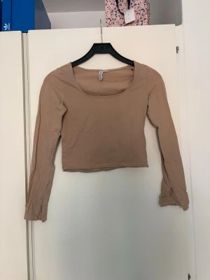 Beige croppad långärmad topp - Trendig beige croppad topp med lång ärm och rundad urringning. Tillverkad i mjukt bomullsmaterial som känns skönt mot huden. Perfekt att styla med jeans eller kjol för en clean look.