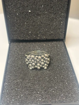 Silverfärgad ring med pärldetaljer - Unik silverfärgad ring med flera små pärlliknande kulor som täcker hela ovansidan. Ringen har en modern och trendig design som sticker ut och passar perfekt för dig som gillar statement-smycken. 