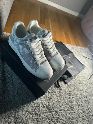 Gråvita sneakers från Numeris - Snygga sneakers från Numeris med gråvitt kamouflagemönster och vita detaljer. Skorna har klassisk låg profil, vita snören och tåparti i textil. Perfekta för dig som vill ha en stilren och modern look.