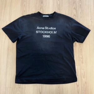 Svart Acne Studios t-shirt Stockholm - Svart t-shirt från Acne Studios med tryck 'Acne Studios STOCKHOLM 1996' på bröstet. Klassisk passform med rund hals och korta ärmar. Perfekt för dig som gillar stilrena och ikoniska plagg från populära märken.