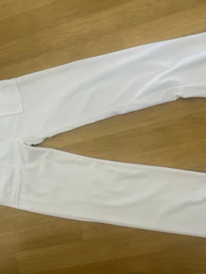 mjukisbyxor  - Säljer ett par vita mjukisbyxor med broderad logga på fickan. Byxorna har raka ben och är gjorda i mjukt, bekvämt material som passar perfekt för chill dagar. Snygg minimalistisk design och diskret detalj vid fickan.