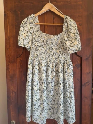 Blommig klänning med smock & puffärmar - Söt kortklänning med blommigt mönster i vitt och ljusgult på ljus botten. Klänningen har puffärmar, smockad överdel och en luftig kjol. Perfekt för sommarens varma dagar och har en romantisk vibe.