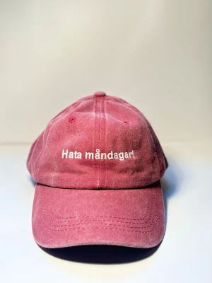 Keps ”hata måndagar” röd - Den där känslan när väckarklockan ringer och själen lämnar kroppen. “Hata måndagar” är kepsen för dig som inte ens låtsas gilla starten på veckan.  Tillverkad i 100% ekologisk bomull så du åtminstone har det skönt när resten suger.