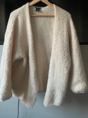 Beige stickad kofta från Lindex - Mysig och oversized beige stickad kofta från Lindex. Koftan har en öppen front utan knappar, långa ärmar och en fluffig, mjuk struktur. Perfekt att slänga över en t-shirt för en avslappnad look. Supersnygg och trendig❣️