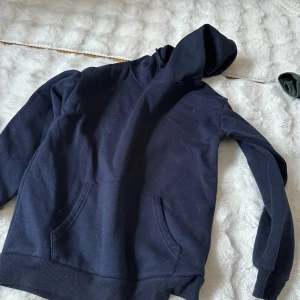 Mörkblå hoodie med huva - Säljer en enkel och stilren mörkblå hoodie med stor känguruficka framtill och klassisk huva. Hoodien har ribbade muddar vid ärmslut och nederkant. Perfekt för en avslappnad och bekväm stil.