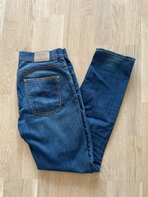 Blå Nudie jeans Grim Tim W33 L32 - Jag säljer dom här riktigt feta Nudie jeansen i modellen Grim Tim. De är inte använda mycket och är i fint skick. Tveka inte att höra av er!       Mått: Längd=105cm. Midja=43cm