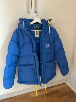 Blå Fjällräven Expedition dunjacka - Säljer nu min fjällrävenjacka nu när vintern är över och den har gjort sitt! Små skavanker finns, enstaka fläckar och en defekt på vänster arm (se bild) därav pris!! Ej tvättad, de små fläckarna går säkert att få bort men har inte provat. I övrigt fint skick, VARM, snygg och gosig!! Kom gärna med prisförslag 💙