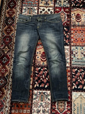 Mörkblå slim fit jeans med slitningar - Säljer ett par mörkblåa Dondup slim fit jeans med snygga slitningar och kontrastsömmar. Jeansen har klassiska fem fickor och coola detaljer på bakfickorna. Perfekt för dig som gillar en trendig och avslappnad look. Längd från midjan till slutet på jeansbenen är: 90cm