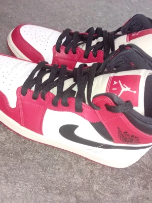 Air Jordan 1 Retro röd/vit/svart - Säljer ett par klassiska Air Jordan 1 Retro sneakers i färgerna röd, vit och svart. Skorna har högt skaft, svart swoosh och svarta skosnören. Ovandelen är i läder med perforerad tåbox och ikoniska Jordan-loggor på sidan och plösen.