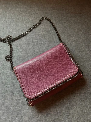 Vinröd axelväska  - Säljer en vinröd axelväska. Väskan har två innerfack och en av dem är med dragkedja. Väskan går ungefär till höften om du har den över axeln. 