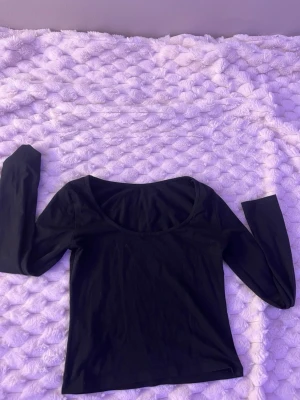 Svart långärmad topp med rund hals - En enkel och stilren svart långärmad topp med rundad urringning. Perfekt att matcha med jeans eller kjol för en clean look. Tunn och mjuk i materialet, sitter snyggt och är lätt att bära till olika outfits.