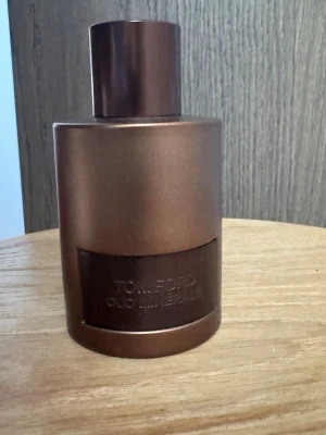 Tom Ford Oud Minérale parfym - Tom Ford Oud Minérale parfym i en elegant, mörkbrun metallisk flaska med rund form och matchande lock. Flaskan har en stilren design med en präglad etikett framtill. Perfekt för dig som gillar exklusiva dofter och snygg förpackning.