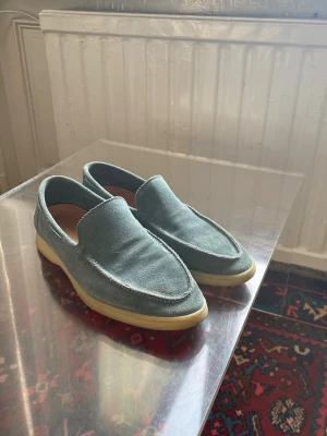 Blå loafers från Aurélien  - Säljer ett par ljusblå loafers i mocka med klassisk design och ljus. Skorna passar lika bra på uteserveringen som i båten. Skorna är köpta för ca 1 månad sedan, men har inte använts eftersom de är för små för mig. Det förekommer inga synliga defekter. Ny pris: 3 920kr. 