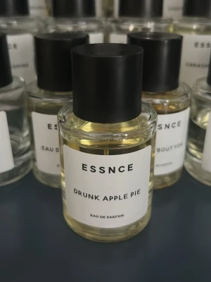ESSNCE Drunk Apple Pie parfym - ESSNCE Drunk Apple Pie Eau de Parfum i en rund, genomskinlig glasflaska med svart cylinderformad kork. Doften har en modern och minimalistisk etikett i vitt med svart text. Perfekt för dig som gillar fruktiga och söta doftnoter.