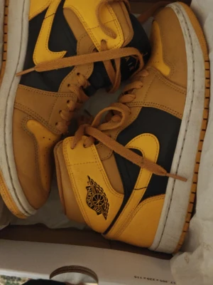 Air Jordan 1 mid gul och svart - Säljer ett par Air Jordan 1 High sneakers i en cool gul och svart färgkombination. Skorna har klassisk Jordan-logga på sidan och är tillverkade i läder med perforerad tå för extra komfort. Perfekt för dig som vill sticka ut med ett ikoniskt sneaker-utseende.