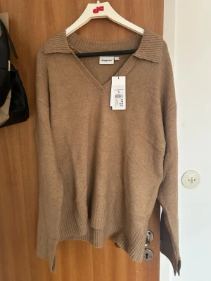 Beige stickad tröja med krage Kappahl - Stickad tröja i beige från Kappahl med v-ringning och bred krage. Tröjan har långa ärmar och ribbade muddar vid ärmslut och nederkant. Perfekt för lager på lager och enkel att matcha till olika outfits.