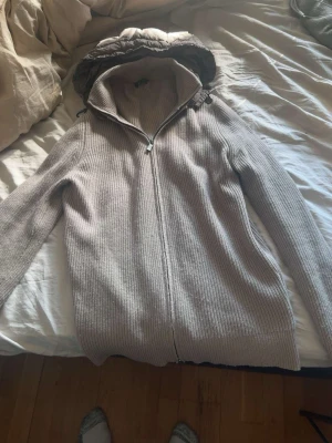 Beige stickad hoodie Massimo Dutti - Ribbstickad beige tröja med dragkedja från Massimo Dutti. Tröjan har en stor huva med vadderad insida och dragsko. Tillverkad i mjukt material, perfekt för kyliga dagar. Enkel och stilren design som passar till det mesta.