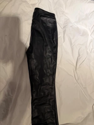 Svarta skinnbyxor med rak passform - Snygga svarta byxor i skinnimitation med rak passform. Byxorna har en slät yta och mjuk insida, perfekta för att lyfta vilken outfit som helst. Klassisk midja och minimalistisk design utan synliga detaljer.