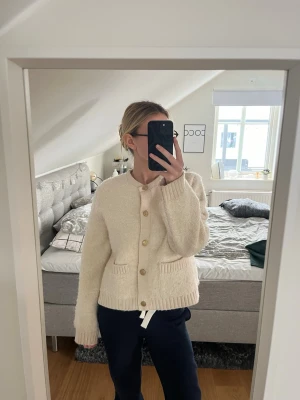 Beige stickad kofta med knappar - Mysig beige stickad kofta med rund hals och träknappar framtill. Koftan har två fickor och ribbade muddar vid ärmslut och nederkant. Perfekt för lager-på-lager och chill dagar.