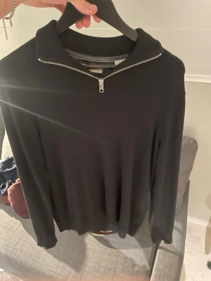 Svart tröja med halvzip och krage - Snygg svart tröja med halvzip och krage. Tröjan har långa ärmar och är tillverkad i ett mjukt material som känns skönt mot huden. Perfekt för en stilren och avslappnad look. 