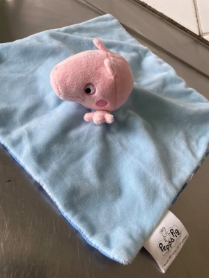 Snuttefilt Peppa Pig blå/rosa alltså 2 st olika  - Mysig snuttefilt med Peppa Pig-figur i mjuk plysch. Ena sidan är ljusblå och andra sidan rosa, med en liten Peppa Pig i rosa plysch fastsydd i mitten. Perfekt som gosedjur eller trygghetsfilt för små barn. 2 st en rosa och en blå snuttetrasa 