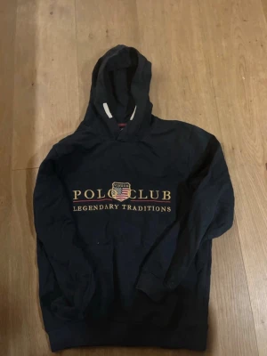 Polo Club tröja - Snygg mörkblå hoodie från Vinson Polo Club med broderad logga och texten 'Legendary Traditions' på bröstet. Klassisk huva och magficka framtill. Perfekt för en avslappnad och sportig stil.