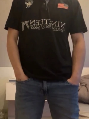 Svart t-shirt från Polo Ralph Lauren - Snygg svart t-shirt från Polo Ralph Lauren med tryck framtill, amerikansk flagga och logga på bröstet. Klassisk passform och korta ärmar. Perfekt till jeans för en clean och stilren look.