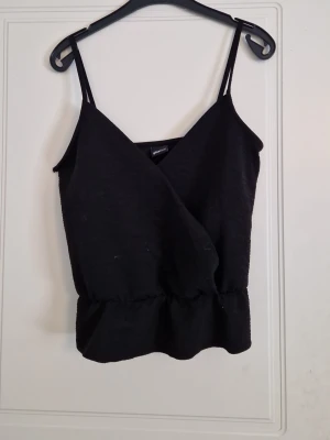 Svart omlott linnetopp - Snygg svart omlott linnetopp med smala axel overarching och resår i midjan. Perfekt för att styla med jeans eller kjol. Enkel men trendig design som passar till många olika looks.