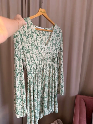 Grön och vit omlottklänning  - Super snygg klänning! Klänningen har v-ringning, långärmad design och markerad midja som ger en snygg siluett. Perfekt för dig som gillar trendiga och bekväma plagg. Stretchiga material. 