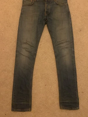 Blå slim fit jeans med slitningar - Snygga blå slim fit jeans med lätt slitna detaljer och klassisk femficksdesign. Jeansen har en smal passform och är tillverkade i denim med en något tvättad look. Perfekta för en avslappnad och trendig stil.