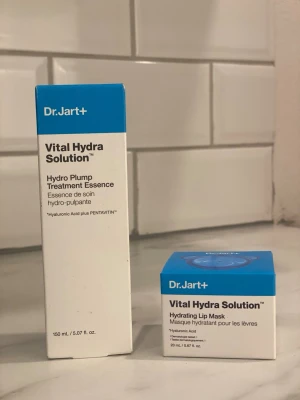 Dr.Jart+ Vital Hydra Solution set - Dr.Jart+ Vital Hydra Solution set med Hydro Plump Treatment Essence (150 ml) och Hydrating Lip Mask (20 ml). Båda produkterna återfuktar huden och läpparna med hyaluronsyra. Förpackningarna är vita med blå detaljer och modern design.