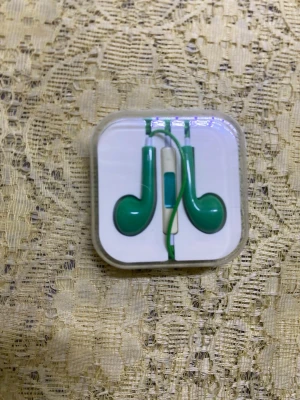 Gröna in-ear hörlurar med mikrofon - Snygga gröna in-ear hörlurar med sladd och inbyggd mikrofon. Kommer i ett vitt plastetui som håller dem på plats. Perfekta för musik, poddar eller samtal. Sladden är också grön och hörlurarna har en klassisk rundad form.